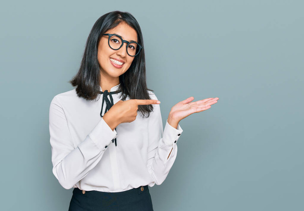 Bella asiatica giovane donna indossa business shirt e occhiali stupito e sorridente per la fotocamera, mentre si presenta con mano e puntando con il dito.  - Foto, immagini