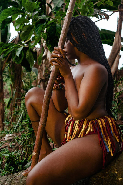 Mujer negra nativa sentada en tronco mientras espera - Foto, afbeelding