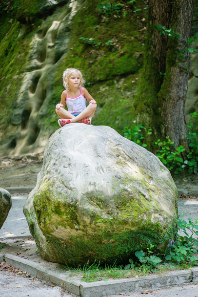 niña se sienta en piedra grande
 - Foto, imagen