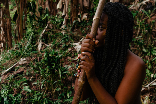 Mujer negra de selva sentada, reposada en su arma mientras piensa - Фото, изображение