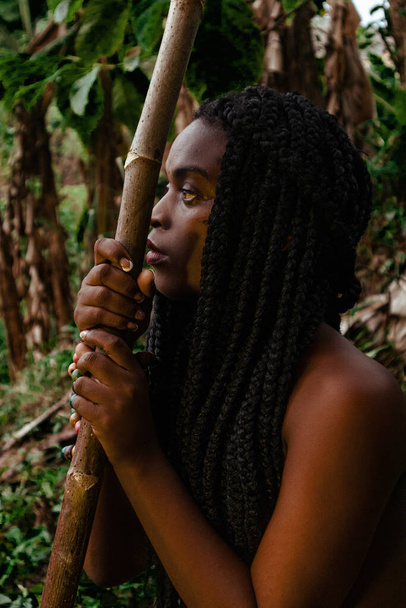 Mujer negra de selva sentada, reposada en su arma mientras piensa - Фото, изображение