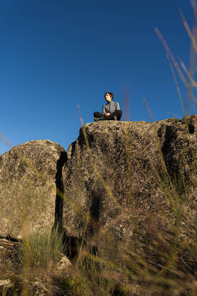 Young and attractive female meditating on top of a rock during a sunny and cold winter morning - Fotografie, Obrázek