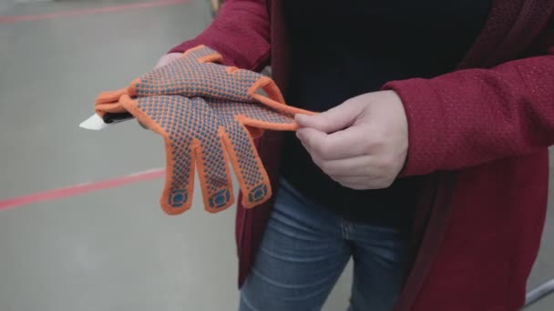 Kobieta w sklepie z materiałami budowlanymi wybiera do kupienia rękawiczki z gumowymi nacięciami - Materiał filmowy, wideo