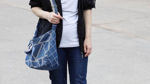 Часть тела женщины в джинсах, которая держит сумку из джинсовой ткани на плече - Фото, изображение