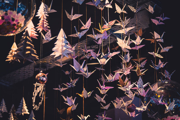Un sacco di origami cigni appesi al tetto, visti da sotto in una stanza dolcemente illuminata - Foto, immagini