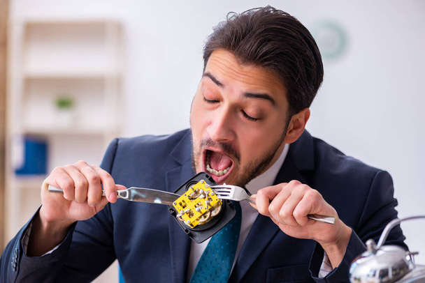 Young businessman employee eating alarm-clock - Фото, изображение