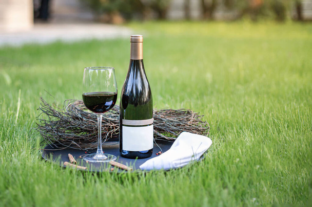 Una bottiglia di vino rosso con un bicchiere pieno si erge sull'erba alla luce della sera - Foto, immagini
