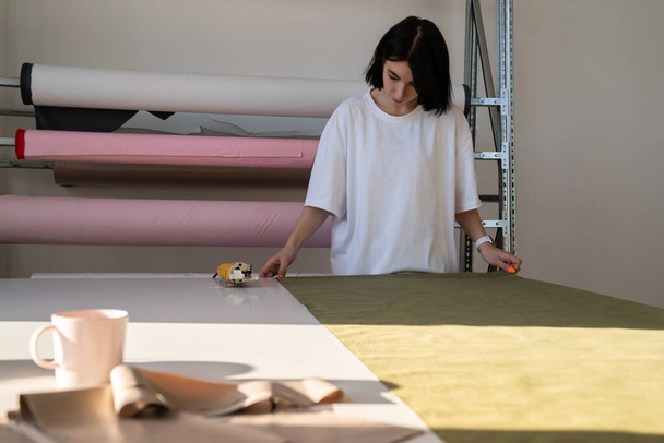 Girl tailor preparing to cut fabric in garment studio. Woman designer work in atelier with material - Fotografie, Obrázek
