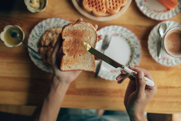 Knife spreading butter on toast bread in hands in the morning breakfast. Coffee and dessert concept. - Photo, Image
