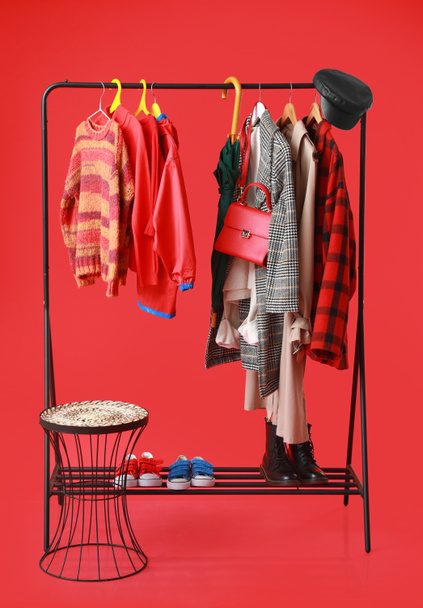 Стойка со стильной одеждой, обувью и аксессуарами на цветном фоне - Фото, изображение