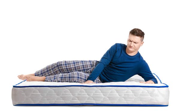 Young man lying on mattress against white background - 写真・画像