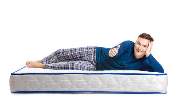 Young man lying on soft mattress and showing thumb-up against white background - 写真・画像