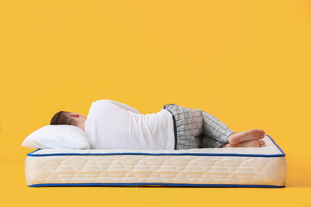 Young man lying on soft mattress against color background - Foto, imagen