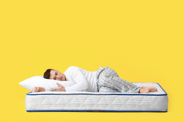 Young man sleeping on soft mattress against color background - Foto, Imagen