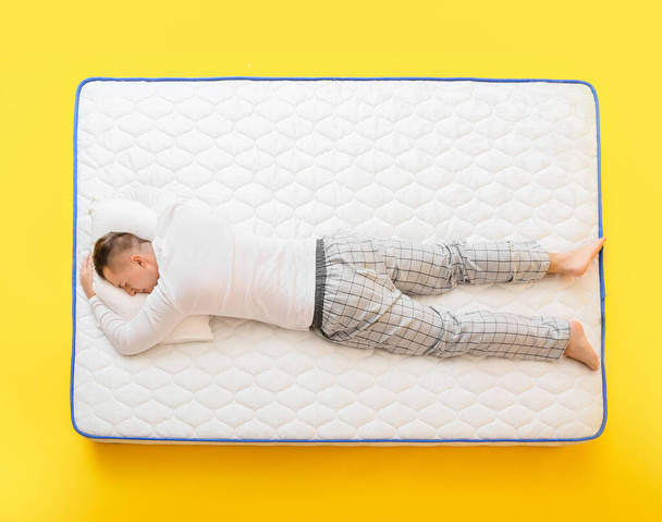 Jongeman slapen op zachte matras tegen kleur achtergrond - Foto, afbeelding