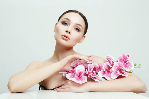 Красивая молодая женщина с цветами. Портрет девушки с орхидеей. Чистое лицо, уход - Фото, изображение