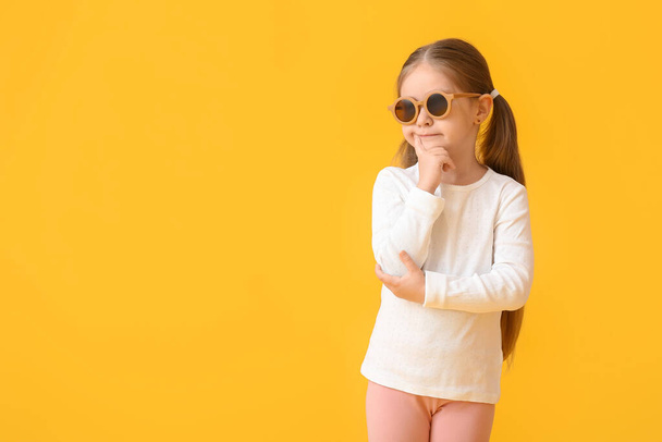 Bedachtzaam klein meisje dragen stijlvolle zonnebril op kleur achtergrond - Foto, afbeelding