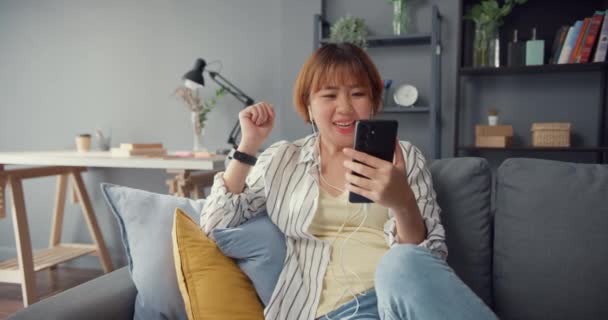 Mladá asijská dáma používající chytrý telefon video hovor mluvit s rodinou na pohovce v obývacím pokoji v domě. Práce z domova vzdáleně během uzamčení covid-19, společenská vzdálenost, karanténa pro prevenci koronaviru. - Záběry, video