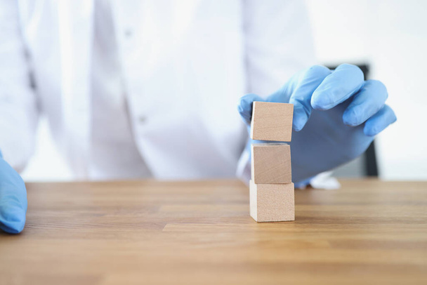 Lékař v rukavicích staví věž z dřevěných kostek - Fotografie, Obrázek