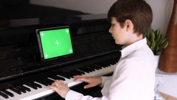 Scuola ragazzo imparare a suonare il pianoforte con tablet app. Bambino divertendosi con imparare a suonare lo strumento musicale. Tablet con schermo verde croma sfondo chiave per la nuova applicazione, commercio e programmi - Filmati, video