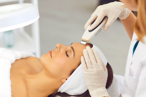 Manos del cosmetólogo haciendo ultrasonido profesional aparato de limpieza facial para mujer - Foto, Imagen