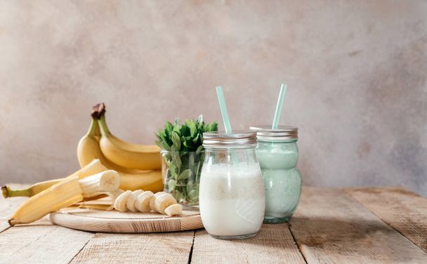 Summer banana smoothie or milkshake with mint and straw in jars on dark wooden table - Фото, изображение