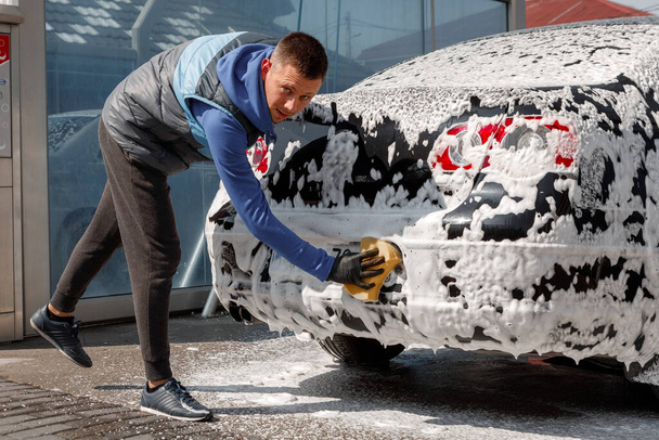 Der Mann wäscht sein Auto in einer Selbstbedienungswaschanlage. - Foto, Bild