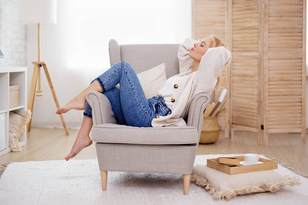 Mooie vrouw ontspannen op fauteuil in lichte woonkamer - Foto, afbeelding
