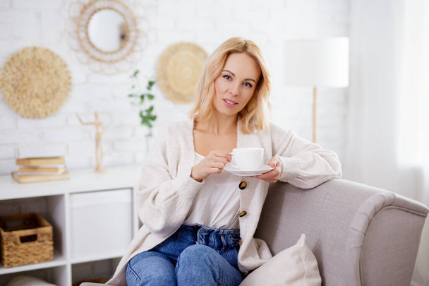 happy woman sitting on armchair and drinking coffe - Foto, Imagem
