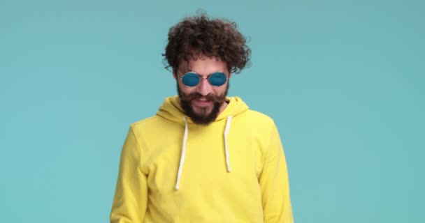 chico barbudo casual fresco con gafas de sol y sudadera amarilla señalando los dedos, baile callejero y divertirse en el estudio - Metraje, vídeo