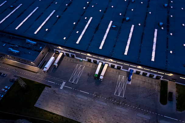 Légi felvétel az áruraktárról éjszaka. Logisztikai központ ipari város zóna felülről. Légi felvétel teherautók rakodásáról a logisztikai központban. Kilátás a drónról. - Fotó, kép