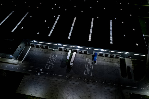 Nacht Luftaufnahme des Warenlagers. Logistikzentrum im Industriegebiet von oben. Luftaufnahme der LKW-Beladung im Logistikzentrum. Blick von der Drohne. - Foto, Bild