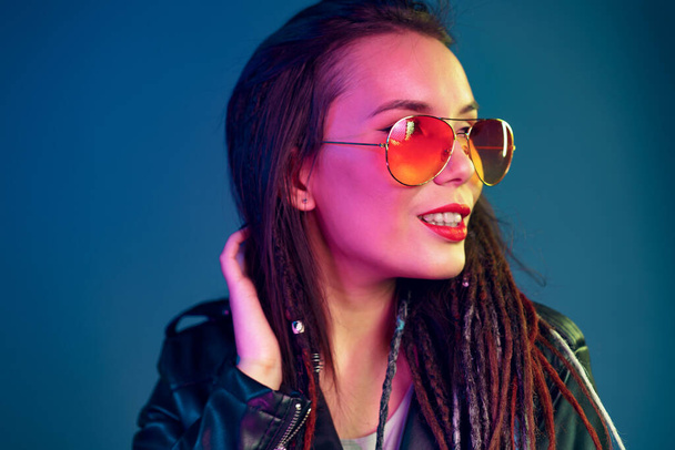 Asian girl in sunglasses and black leather jacket posing against dark blue background - Foto, immagini