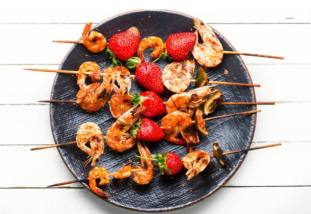 Crevettes grillées appétissantes sur des brochettes en bois avec des fraises. - Photo, image