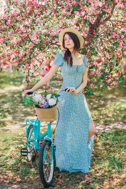 Beautiful girl in blue dress walk with bicycle in blooming spring garden - Foto, Bild
