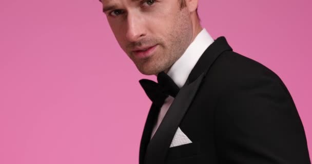 vista laterale di elegante uomo d'affari in smoking nero carte da gioco, presentando asso e re e scommettendo su sfondo rosa in studio - Filmati, video