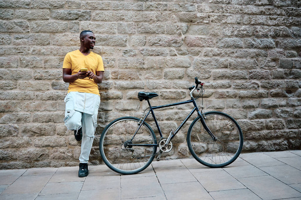 joven hombre negro usando su teléfono inteligente con bicicleta - Foto, Imagen