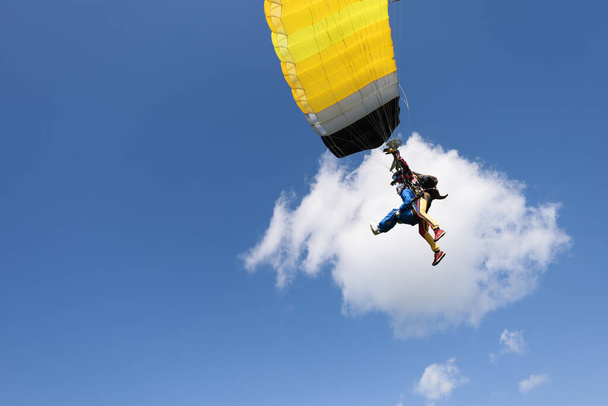 Fallschirmspringen. Tandemsprung. Ein hübsches Mädchen, ihr Lehrer und ein großer gelber Fallschirm. - Foto, Bild