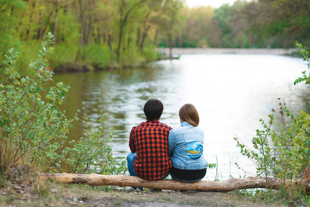 ζευγάρι κάθεται στο κούτσουρο στη λίμνη ακτή και απολαμβάνοντας θέα - Φωτογραφία, εικόνα