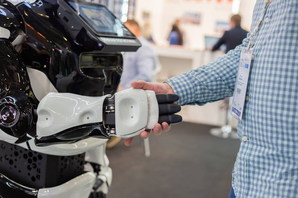 Moscow, Russia - 14 april 2021 : An exhibition visitor shakes hands with an intelligent robot at one of the stands at the International exhibition of transport and logistics services - 写真・画像