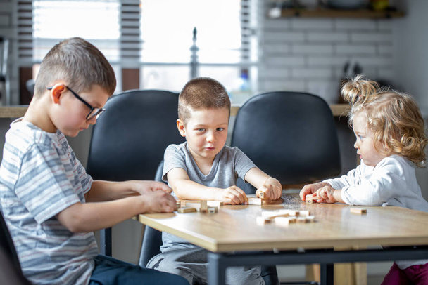 Маленькие дети играют в настольную игру с деревянными кубиками дома на кухне. - Фото, изображение