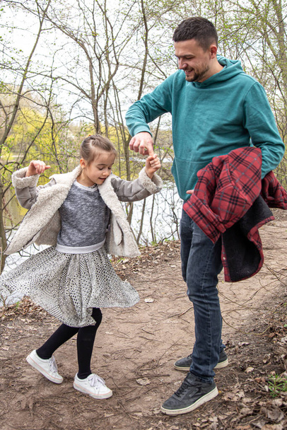 Pikkutyttö on pyörre, joka pitää isäänsä kädestä ja kävelee metsässä.. - Valokuva, kuva