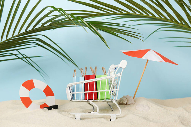 Летние сумки в корзине на пляже с песком, бумажными принадлежностями и пальмовыми листьями - Фото, изображение