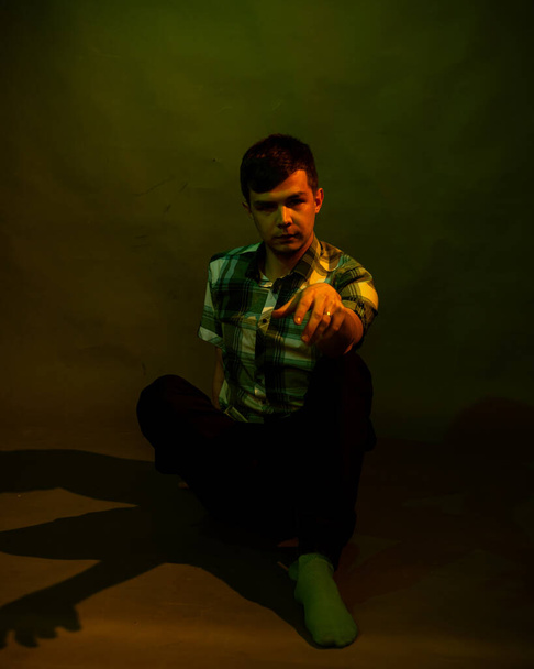 A young man sits on the floor. illuminated by multicolored light - Foto, imagen