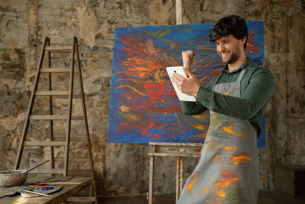 Male artist standing in his studio using a tablet wins. Workshop with oil painting - Fotoğraf, Görsel