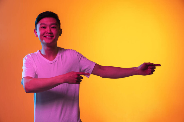 Ritratto di giovane asiatico isolato su sfondo giallo arancio in luce al neon. - Foto, immagini