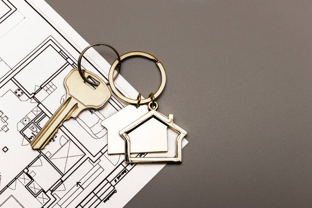 Asunto- ja vuokra-asuntojen ja kiinteistöjen käsite. Kiinnelainat. Metalli avaimenperä muotoinen talo, jossa avain suunnitelmaan talon. Talon ostaminen - Valokuva, kuva