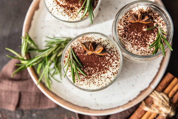 Layered dessert in glass jar with cookie crumble and whipped cream decorated with rosemary and anise, dark background. No bake cheesecake, trifle or pudding. Top view. - Фото, зображення