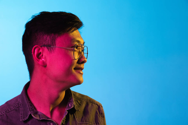 Porträt eines asiatischen jungen Mannes isoliert über blauem Hintergrund im Neonlicht. - Foto, Bild