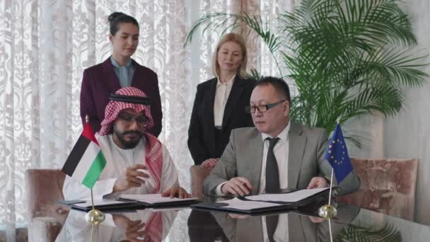 Média lentidão dos Emirados Árabes Unidos e representantes políticos asiáticos sentados à mesa da conferência assinando papéis enquanto suas assistentes femininas estão atrás deles controlando o processo - Filmagem, Vídeo